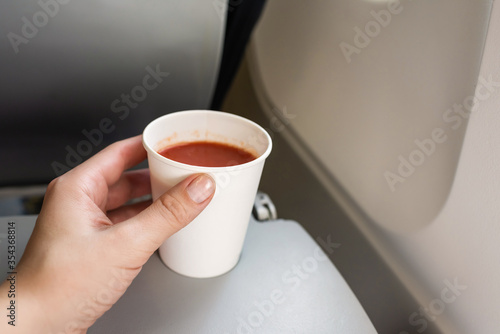 Bild auf Leinwand .Woman passenger holding paper cup of tomato juice sitting in the plane armchair