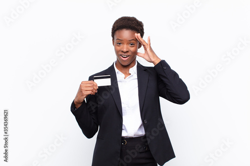 young pretty black womanlooking happy, astonished and surprised, smiling and realizing amazing and incredible good news holding a credit card photo