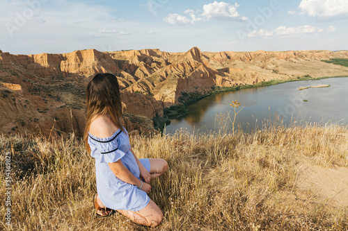 Girl in blue dress looking at the water canyon. Dry rocky landscape. Water canyon and rock erosion.