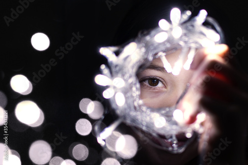 Fototapeta Naklejka Na Ścianę i Meble -  young girly eye looking through chrismas lights, close up portrait with christmas lights
