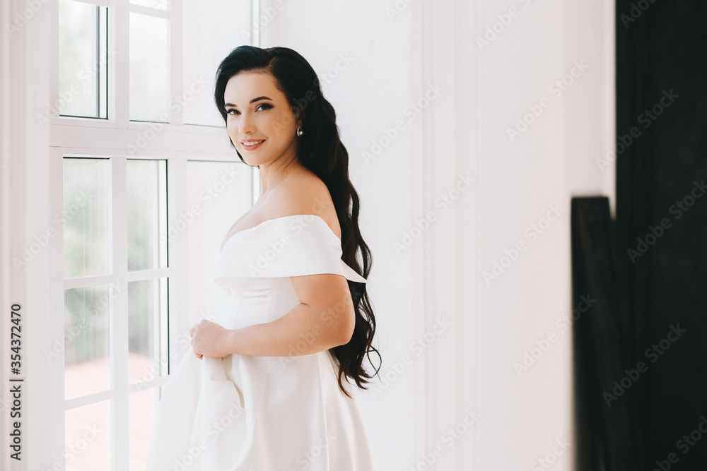 Beautiful bride is a young brunette of European appearance. Large single portrait with a bouquet of flowers. Wedding makeup and hairstyle. Model. In a bright studio by the window. Beautiful bride is a young brunette of European appearance. Large single portrait with a bouquet of flowers. Wedding makeup and hairstyle. Model. In a bright studio by the window.