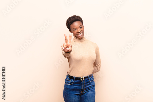 young pretty black womansmiling and looking happy, carefree and positive, gesturing victory or peace with one hand photo