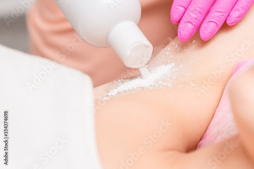 Close up of hand of beautician applying talcum powder on a armpit of woman before the depilation or epilation procedure.