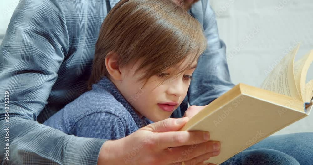 Close up portrait of a little boy with dad reading an interesting book together at home