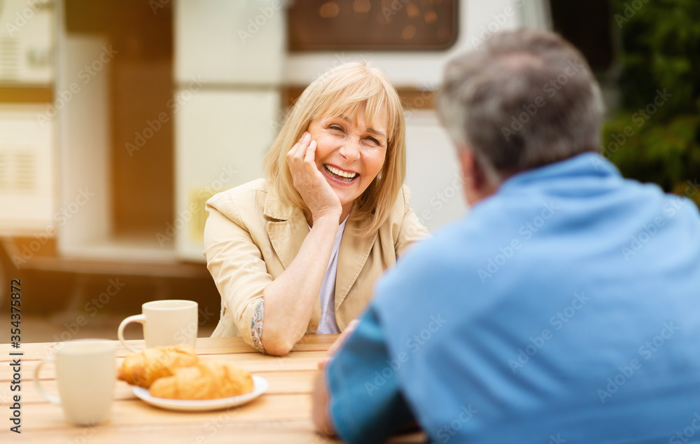 Mature woman talking to her husband during tasty breakfast with coffee and croissants at campground Mature woman talking to her husband during tasty breakfast with coffee and croissants at campground
