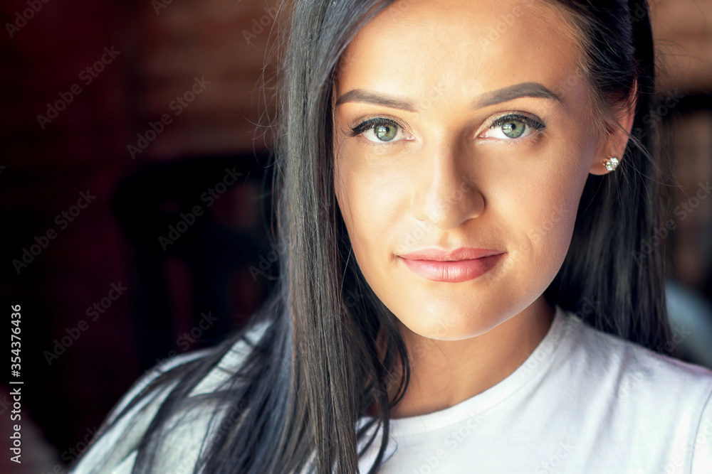 Portrait of a young woman with dark long hair smiling and looking at camera indoor. Portrait of a young woman with dark long hair smiling and looking at camera indoor.