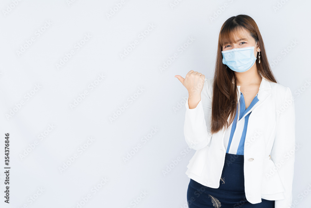 Smiling Asian business woman wearing a medical face mask and pointing finger to side blank space over grey background. Back to the normal concept. Smiling Asian business woman wearing a medical face mask and pointing finger to side blank space over grey background. Back to the normal concept.