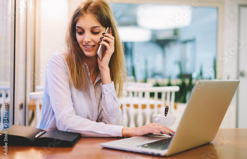 Young female working in coffee shop interior with technology devices