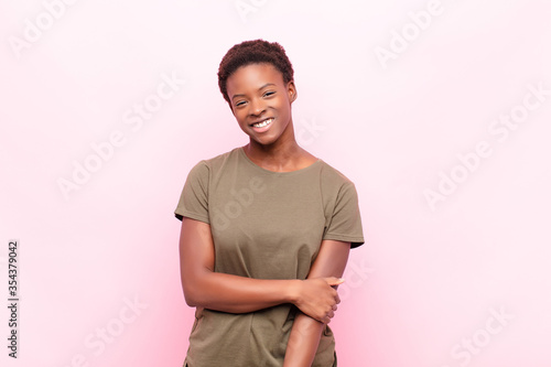 young pretty black womanlaughing shyly and cheerfully, with a friendly and positive but insecure attitude against pink wall photo