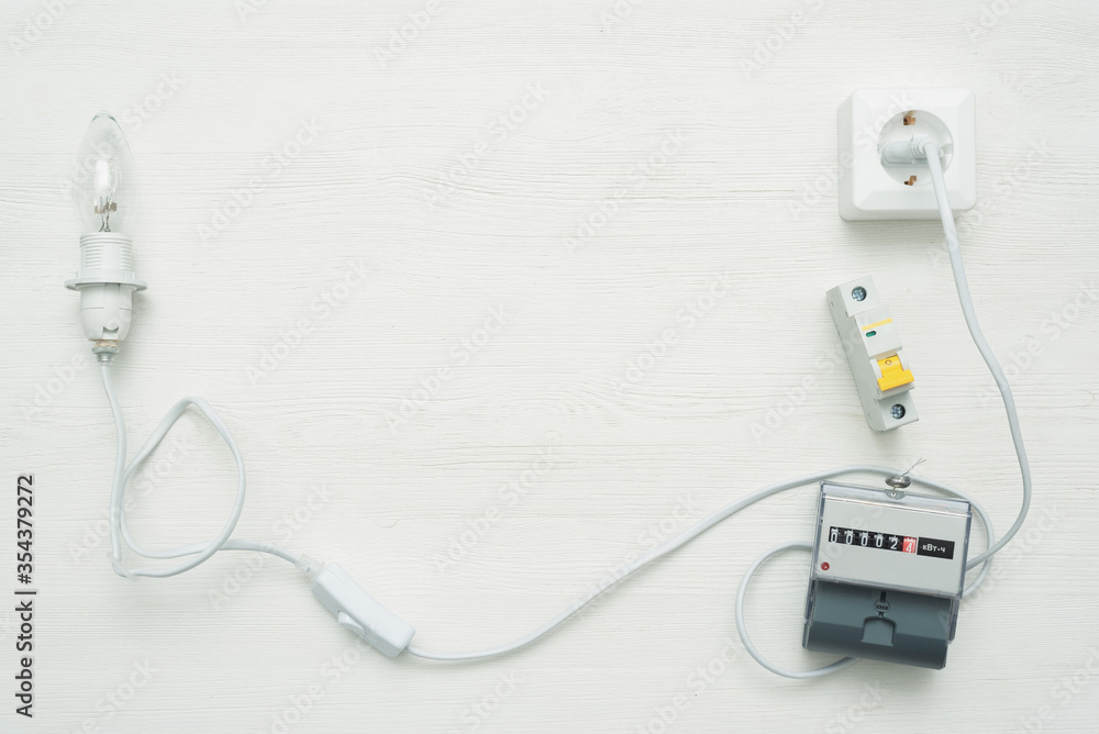 Light bulb with wiring, socket and electric meter on white workbench flat lay background with copy space. Electrical equipment. Light bulb with wiring, socket and electric meter on white workbench flat lay background with copy space. Electrical equipment.
