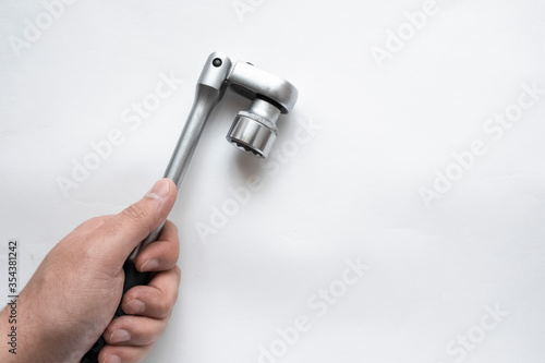 Hand holding flexible-head socket wrench or ratchet on white backdrop. Automotive industry. Repair service concept.