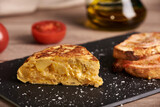 A classic tortilla de patatas, potato omelette snack. The tortilla is on a black plate. Typical spanish food.