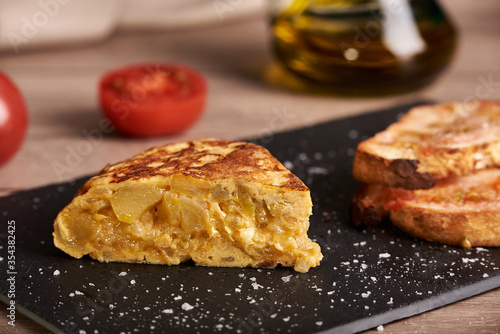 A classic tortilla de patatas, potato omelette snack. The tortilla is on a black plate. Typical spanish food.