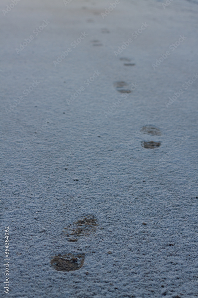 shoeprints on icy ground. Human feet traces, shoes imprints on white snowy road. Fresh snow fallen on asphalt. traces left by man walking away, trajectory of person leaving. several steps shoeprints on icy ground. Human feet traces, shoes imprints on white snowy road. Fresh snow fallen on asphalt. traces left by man walking away, trajectory of person leaving. several steps