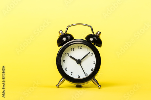 black retro alarm clock on a yellow background,