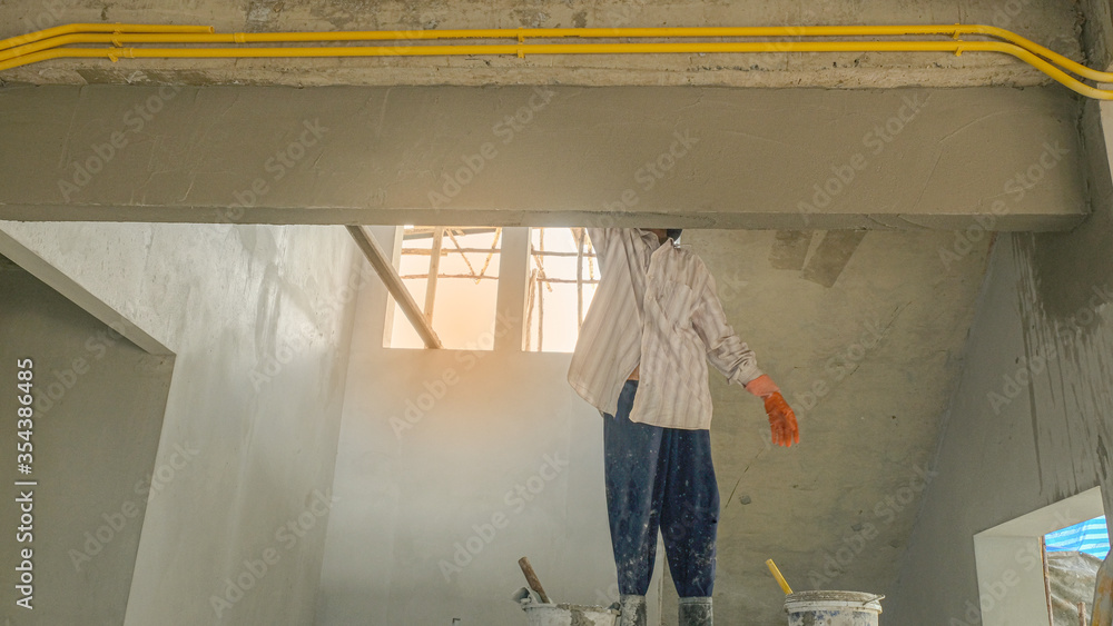 Fototapeta premium female worker plaster liquid cement on wall for new building house. labor mason with orange latex gloves stand on wooden scaffolding use for high level under stair.