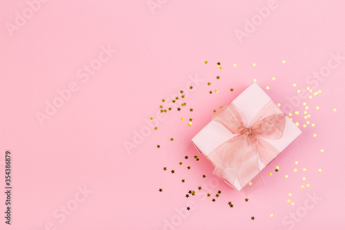 Gift or gift box and stars confetti on a pink table from above. Flat composition for birthday © Nana_studio