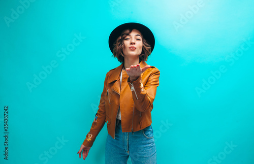Fashion portrait of young stylish hipster woman wearing trendy brown leather jacket, black hat, blue denim jeans and white blank t-shirt . Crazy emotions
