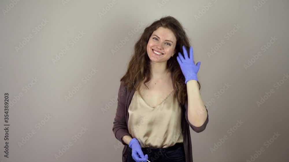 Brunette young woman take off protective mask on face in coronavirus pandemic on grey background blue gloves Brunette young woman take off protective mask on face in coronavirus pandemic on grey background blue gloves