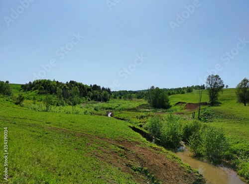 a small river flows among green hilly countryside with trees on a sunny day against a clear blue sky