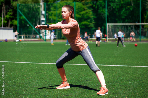 Attractive sporty young woman in sportswear doing stretching exercises on stadium. Fitness woman doing warm up workout.