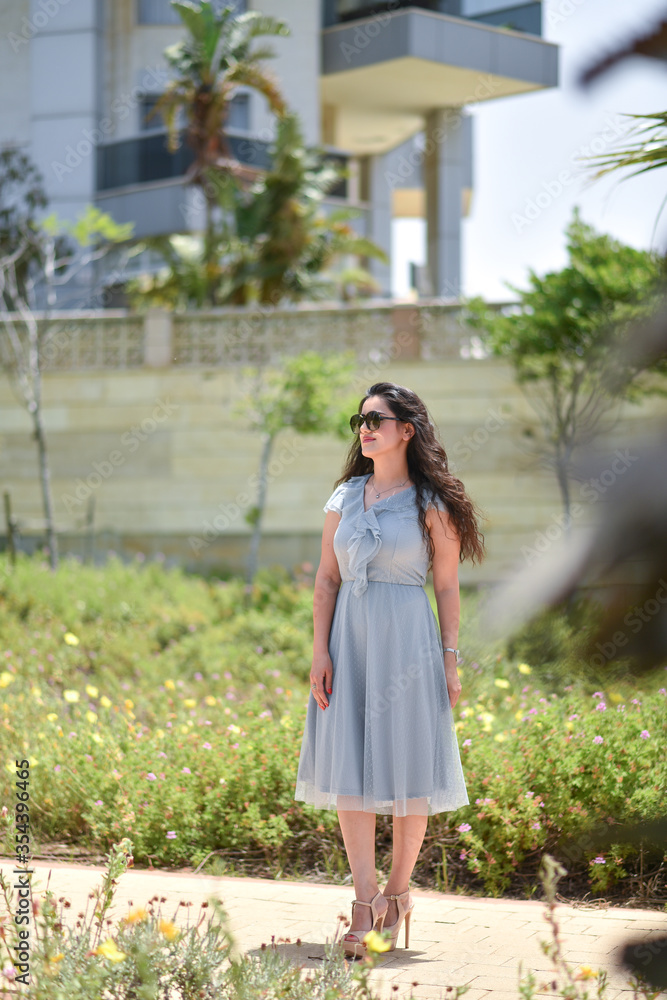 Sexy, pretty young woman on gray dress, fashion sunglasses and blue jeans stand on the grass the background of a green park, looks away. Sexy, pretty young woman on gray dress, fashion sunglasses and blue jeans stand on the grass the background of a green park, looks away.