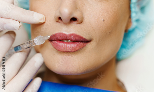 Closeup lips augmentation injections for attractive girl. Plastic surgeon does injection in lip in medical clinic. Cosmetic rejuvenating facial treatment. Empty space for advert