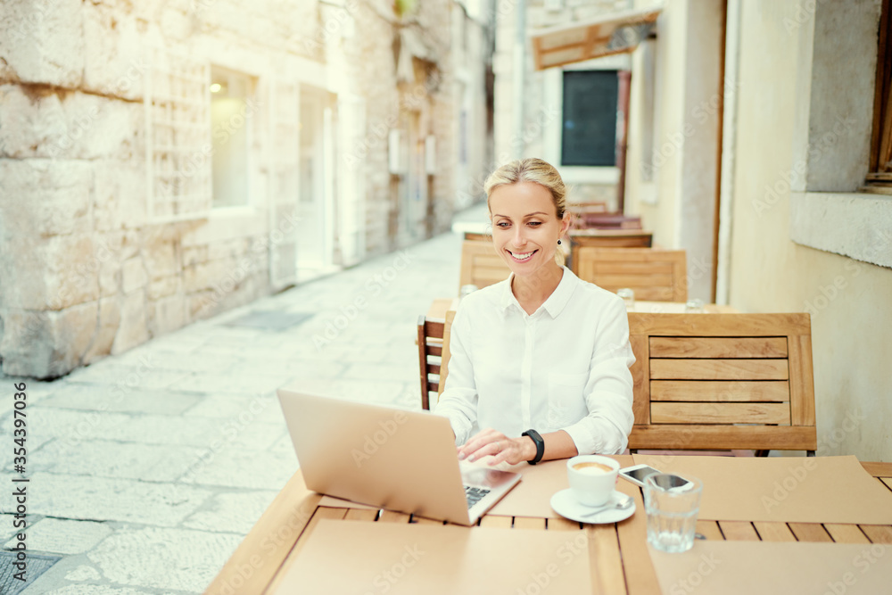 Technology and travel. Working outdoors. Freelance concept. Pretty young woman using laptop in sidewalk cafe on ancient europian street. Technology and travel. Working outdoors. Freelance concept. Pretty young woman using laptop in sidewalk cafe on ancient europian street.