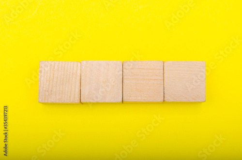 Fototapeta Naklejka Na Ścianę i Meble -  Wooden cubes on a yellow background. Four identical cubes lie on the table horizontally exactly and at an angle