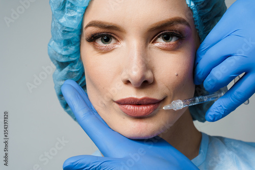 Closeup lips augmentation injections for attractive girl on white background. Plastic surgeon does injection in lip in medical clinic. Cosmetic rejuvenating facial treatment. Empty space for advert