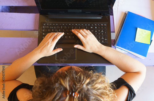 Chica joven rubia escribiendo en un portatil con un cuaderno azul sentada en el suelo, vista cenital y vista lateral photo