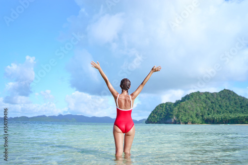 Vacation and freedom. Happy young woman rising hands up standing on tropical beach enjoying beautiful view.