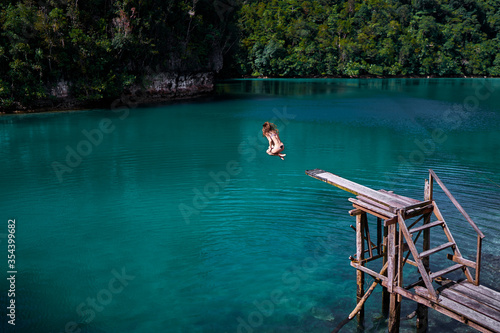 Vacation and activity. Young woman jumping on wooden springboard. Blue tropical lagoon Siargao Island, Philippines.