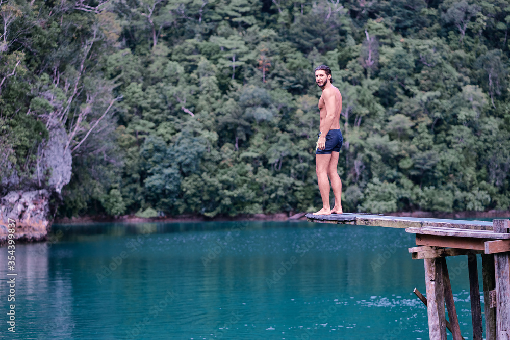 Vacation and activity. Young man enjoying blue tropical lagoon view standing on wooden springboard. Siargao Island, Philippines. Vacation and activity. Young man enjoying blue tropical lagoon view standing on wooden springboard. Siargao Island, Philippines.