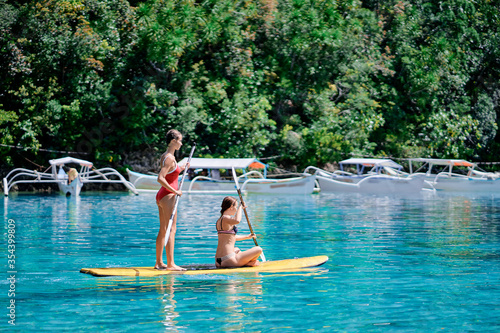 Summer holidays vacation travel. SUP Stand up paddle board. Young women sailing together on beautiful calm lagoon. photo