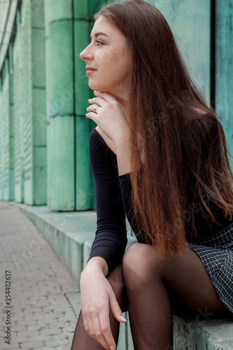 Stylish girl in black sweaters and short skirts posing near the building of the Library of the University of Warsaw. Young woman model appearance with long hair.