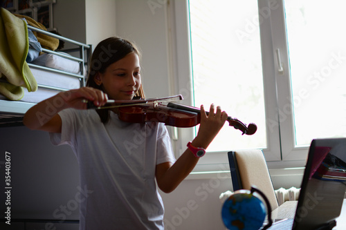 Cute child (little girl) playing violin and exercising at home. Remote learning from home. Video chat conference lesson. Adorable girl with musical instrument.