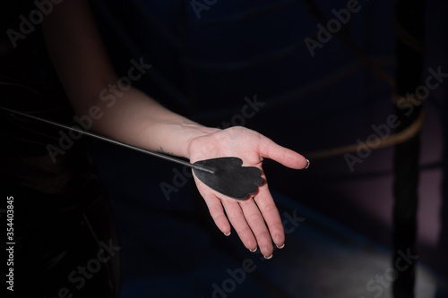 An unrecognizable woman demonstrates an elegant thin leather strip whip in a dark bedroom. Close-up of female hands with a bdsm toy. Pain and pleasure.Adult toy for slaps.