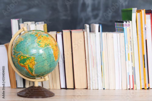 Globe on a chalkboard background. Books arranged vertically in one row on the desk.