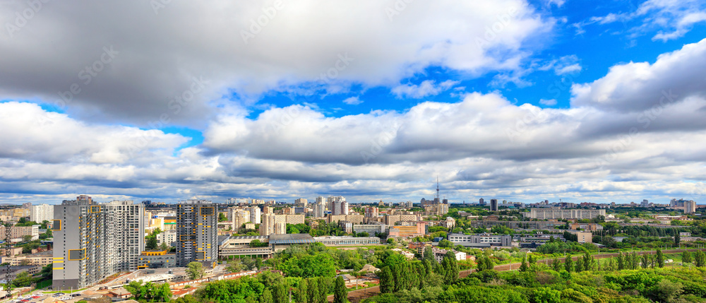 Panorama of cityscape with big low clouds and bright sunlight.