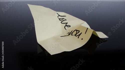 Crumbled handwritten note "love you" on a black shiny surface 