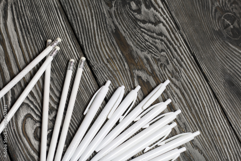 Several ballpoint pens and pencils in white. They lie on brushed pine boards painted in black and white. Several ballpoint pens and pencils in white. They lie on brushed pine boards painted in black and white.