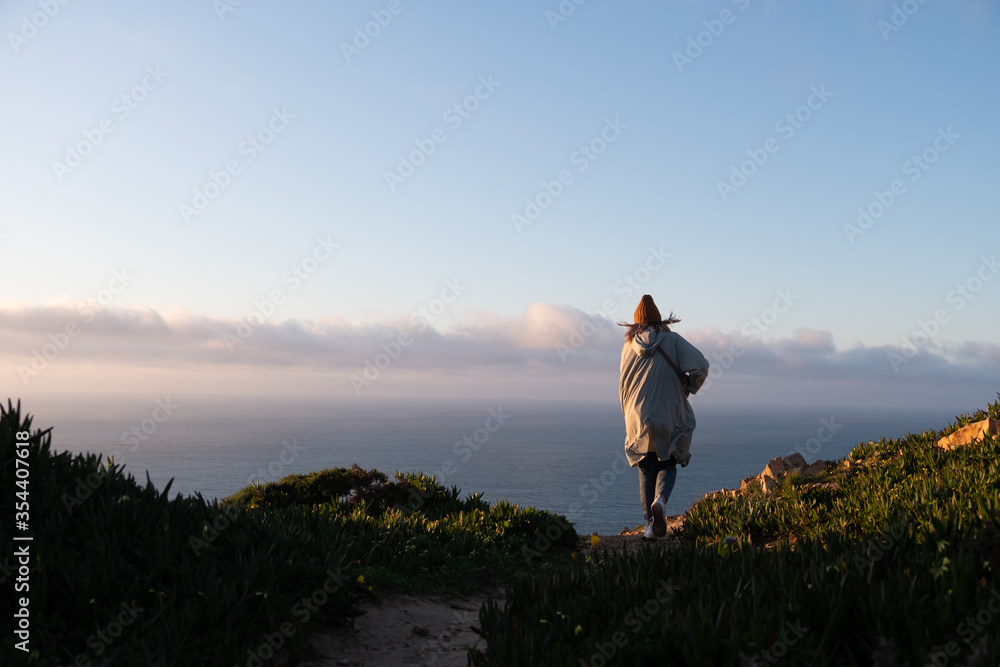 A lone woman walks to the cliff with her cloak fluttering