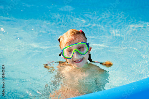 The girl is happily swimming in the pool in a swimming mask. He smiles and looks at the camera.