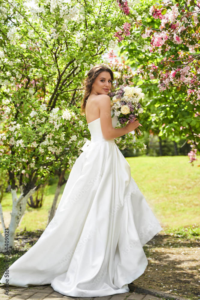 Girl with a bouquet stands at a flowering rose tree, wedding walk Girl with a bouquet stands at a flowering rose tree, wedding walk