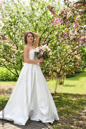 Girl with a bouquet stands at a flowering rose tree, wedding walk