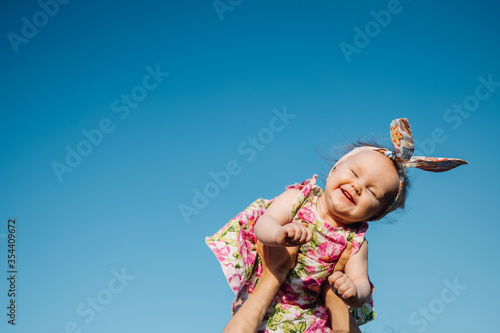 Baby in air. Cheerful child in blue sky background. Infant girl on hands flying in clouds. Fashion child with headwear