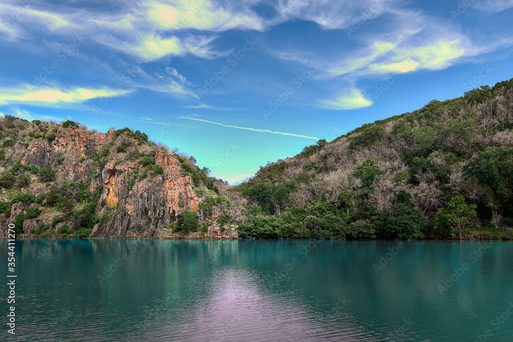 Iron stained cliffs behind Turquoise colored river in texas state park southwest america with whispy clouds in blue sky.