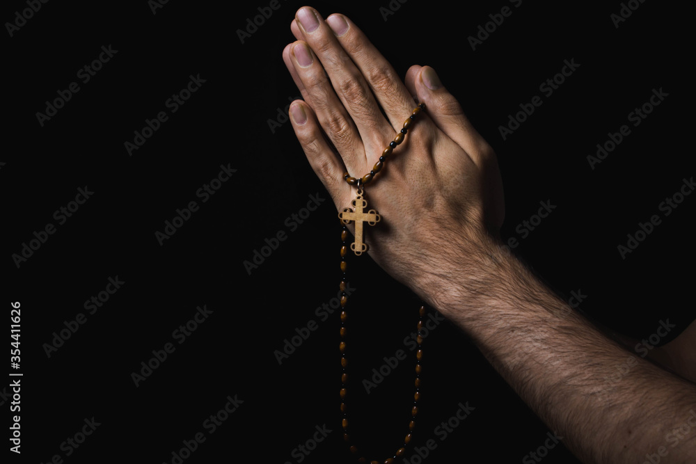 Religion concept. Christian religion. Hands folded in prayer. In the hands of a wooden cross on a wooden chain. Photo on a black background
