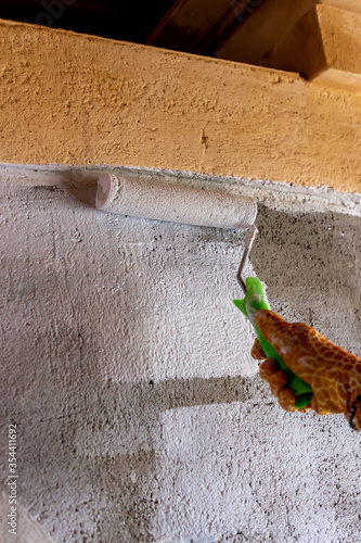 Cement wall painting with white paint and roller. Yellow gloves. photo